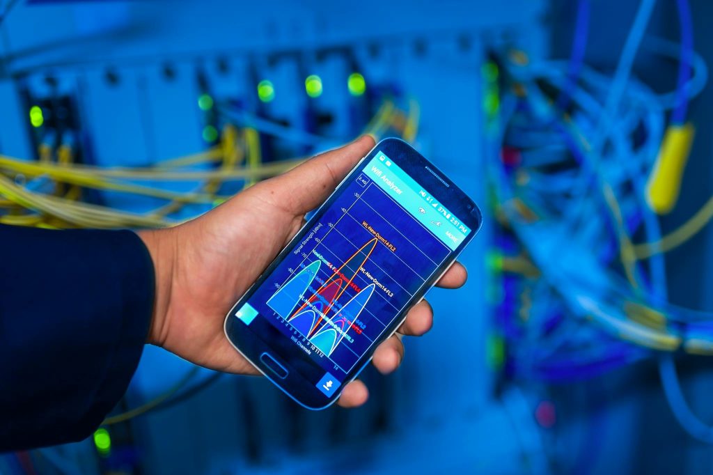 Mobil som viser nettverksanalyse foran nettverksutstyr
